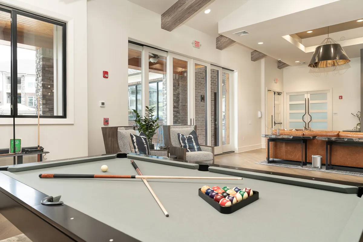 A vibrant lounge setting with a pool table, lounge chairs, large windows, and a bar area. The room exudes a casual, friendly mood ideal for socializing or unwinding after arrival, with contemporary finishes throughout.