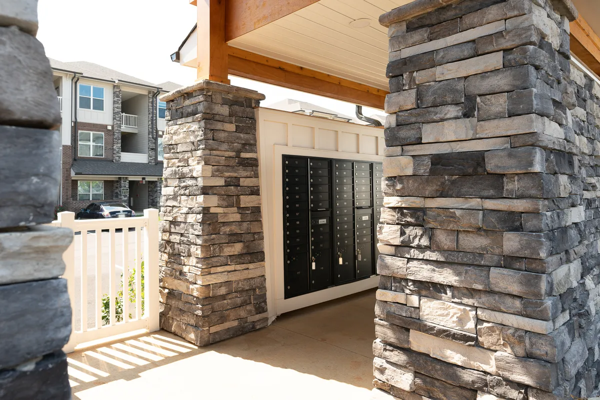 The photo captures the property’s stone columns and mailbox area under an entrance archway, emphasizing daily routines and the ease of access for residents. The setting is both functional and welcoming, with clear paths for coming and going.