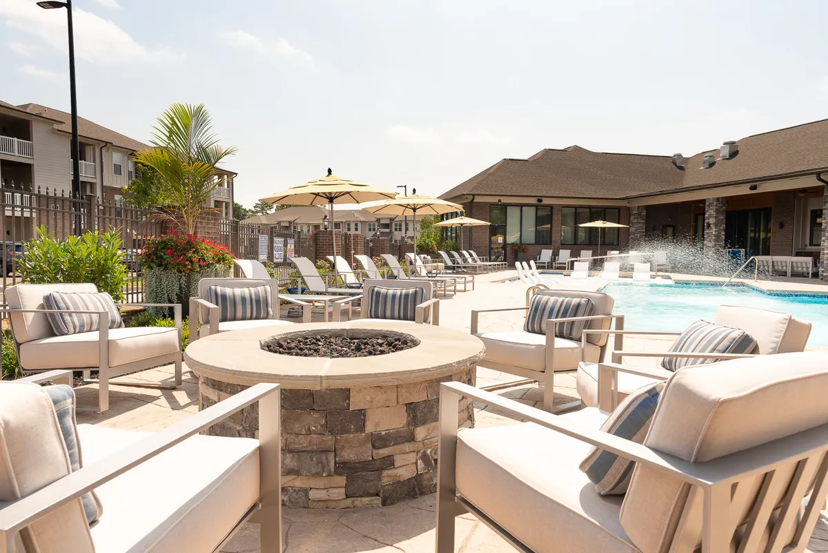 This exterior image showcases a beautifully landscaped pool area with a sparkling swimming pool, comfortable lounge chairs, and a welcoming fire pit surrounded by greenery. The communal space is vibrant yet relaxing, inviting families or groups to gather for sunbathing, socializing, or enjoying quiet moments outdoors.