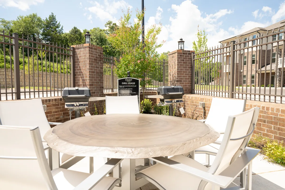 An outdoor communal space is shown with a circular wooden table, white chairs, grills, and surrounding green plants. The area is ideal for outdoor dining, grilling, and family social gatherings, echoing the fun, communal atmosphere referenced in the section.